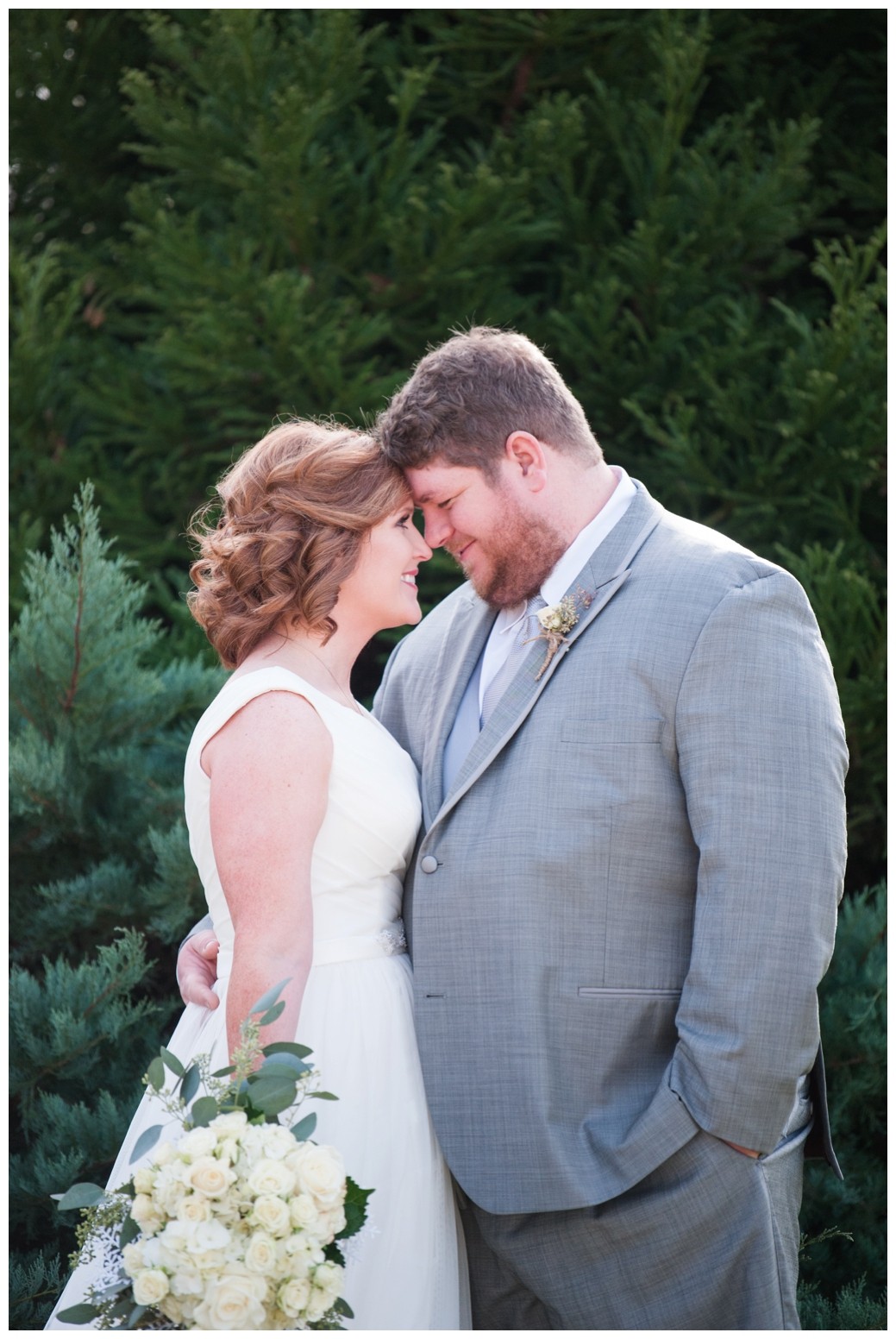 bride and groom smiling with foreheads together in front of greenery