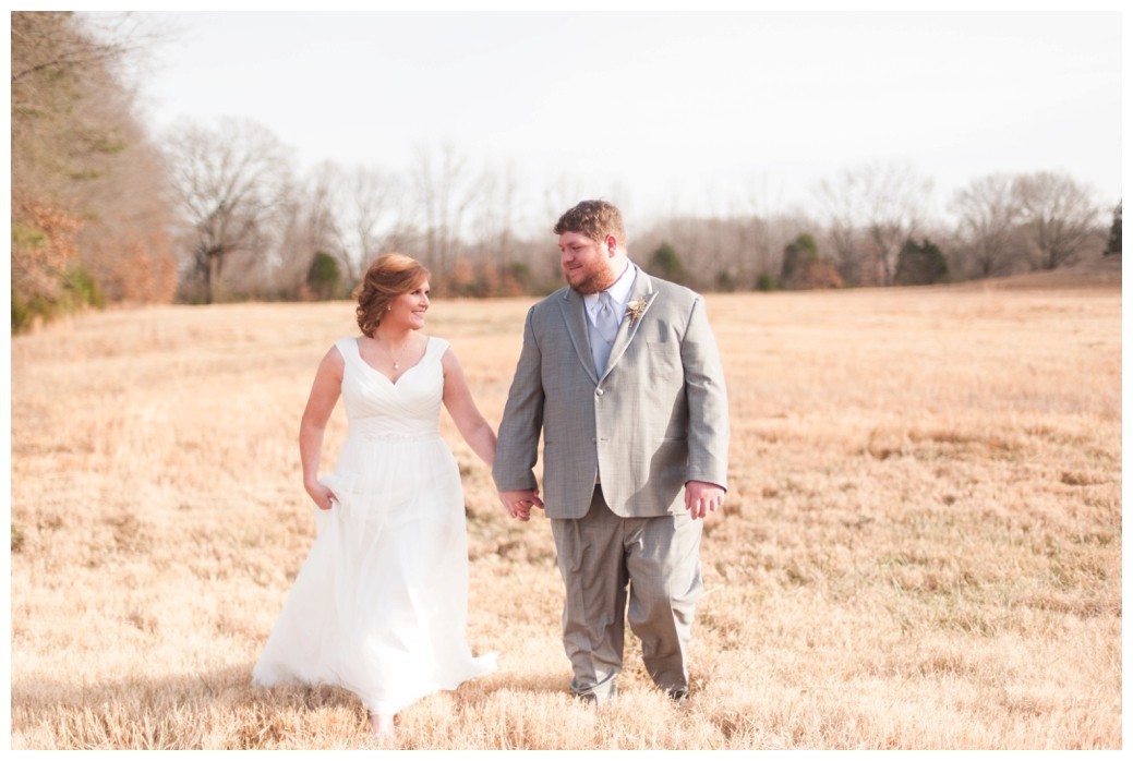 bride and groom walking through field looking at one another