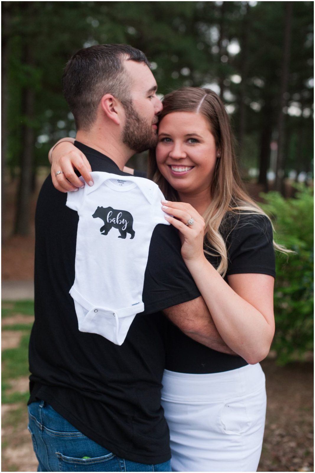 baby announcement parents holding onsie over shoulder