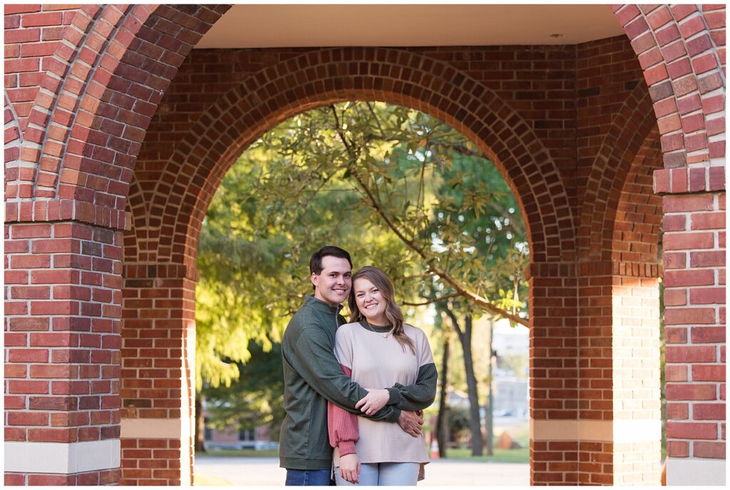 engaged couple stand under a brick arch